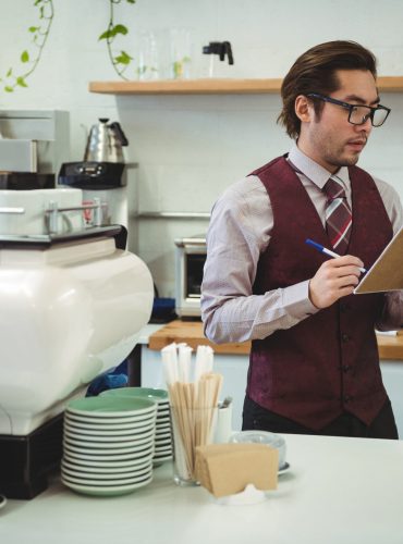 Man writing with pen on clipboard in coffee shop